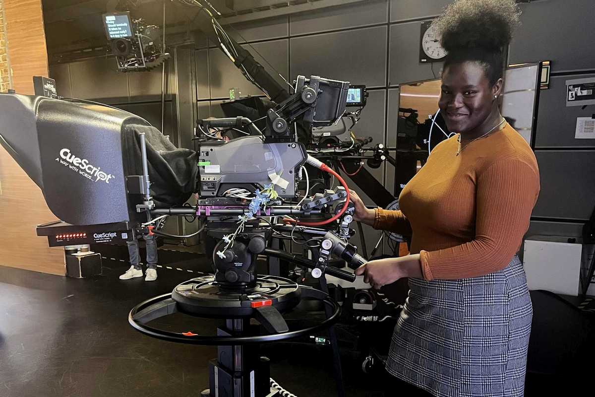 Young woman on work experience at a charity partner poses with a TV camera